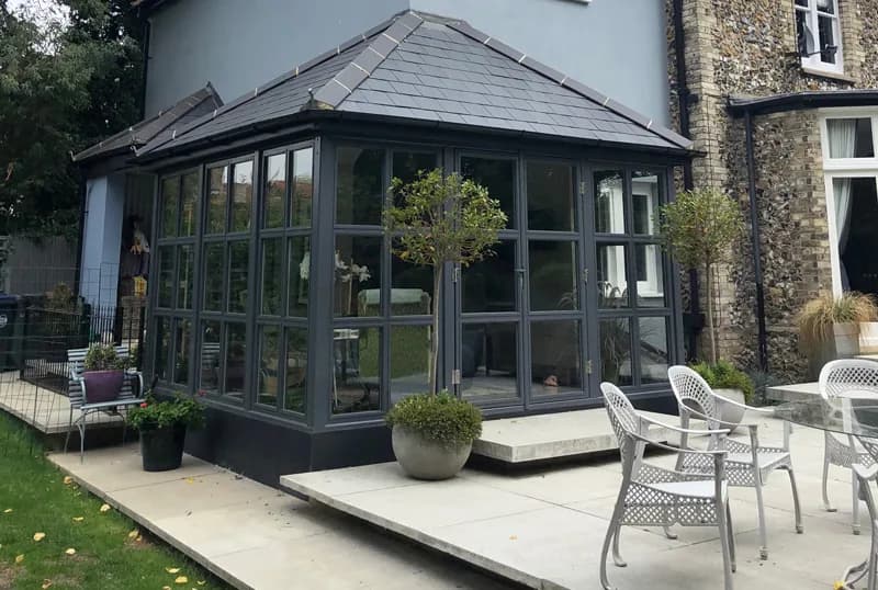 Glass garden room extension on a flint and stone period house, designed to sit quietly against the original building