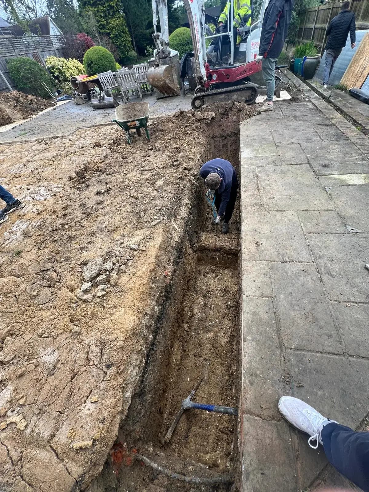 Foundation trench excavated through a patio for a house extension, the stage where ground and drainage issues show up